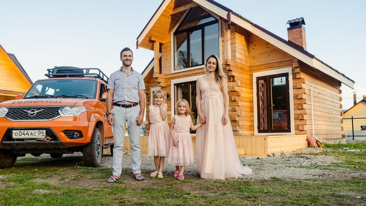 Family of four happily standing outside their modern wooden house on a sunny day.
